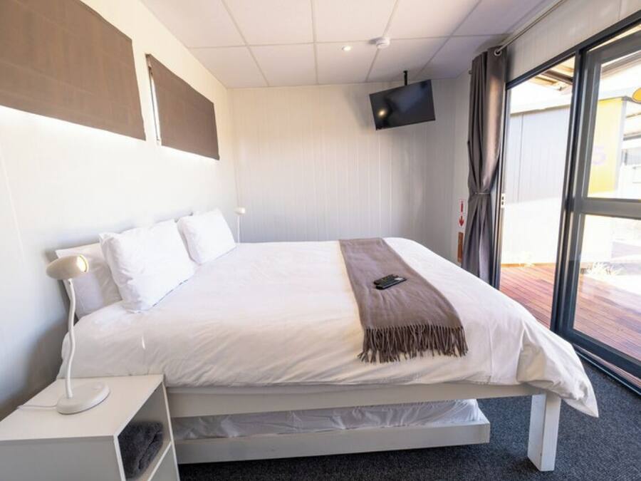 A modern hotel room with a bed, a TV mounted on the wall, and a window with a view.