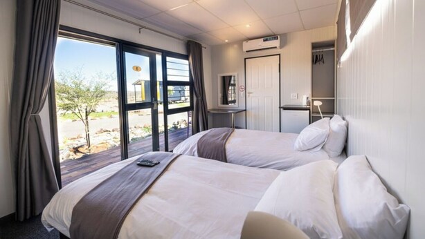 A hotel room with two beds, a desk, a chair, a wardrobe, and a view of the outdoors. - SleepOver Colesberg (Colesberg)