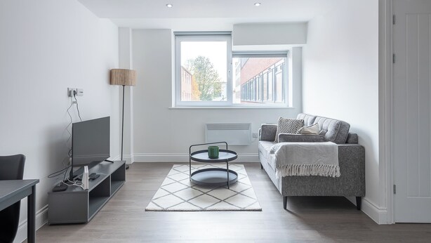 Un salon moderne avec un téléviseur à écran plat, un canapé gris, une table basse et un lampadaire.