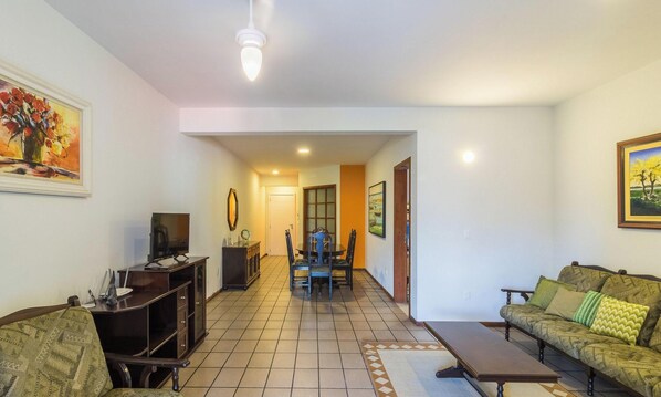 A living room with a sofa, TV, and a dining area with chairs and a table. - Apart w/ BBC 400 m From the Beach Err0104 (Itapema)