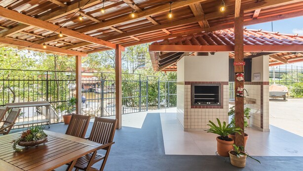 An outdoor patio with a wooden table and chairs, a barbecue grill, and a view of the surrounding area. - Apart w/ BBC 400 m From the Beach Err0104 (Itapema)