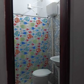 A bathroom with a shower curtain featuring fish patterns, a white toilet, and a sink. - Pousada mambucaba  (Angra dos Reis)