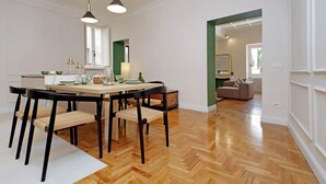 A dining area with a wooden herringbone floor, a round table with chairs, pendant lighting, and a view into a living room with a sofa and a mirror. - Luxury home near Piazza Venezia (Roma)