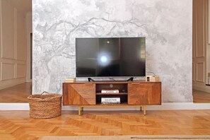Ein modernes Wohnzimmer mit einem großen Flachbildfernseher auf einem Holz-TV-Möbel, einem gewebten Korb und einer Wand mit Marmorstruktur.