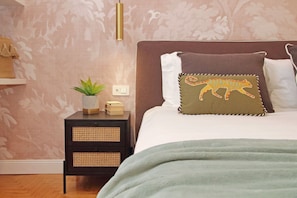 Quarto com uma cama, mesa de cabeceira com uma planta e luminária fixada na parede.