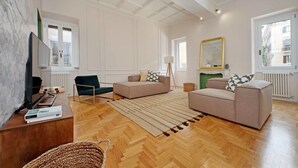 A spacious living room with a wooden floor, two sofas, a coffee table, a TV, and a large mirror. - Luxury home near Piazza Venezia (Roma)