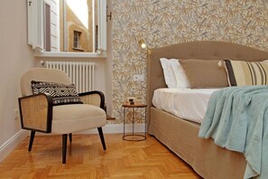 Ein Schlafzimmer mit Bett, Sessel, kleinem Tisch und Heizkörper.