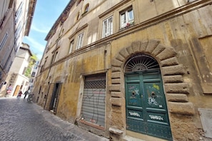Uma rua estreita com edifícios antigos, calçada de pedra e uma porta verde com grafite.