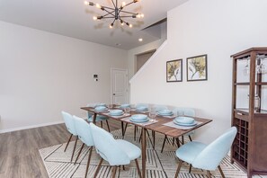 A dining area with a long table set for six, light blue chairs, a wooden floor, and a chandelier. - 4 bed, 3 bath Single Family Home in Millville by the Sea: Community Pool, Fitness Center, Club house, Kayaking, Beach Shuttle, Free WIFI (Frankford)