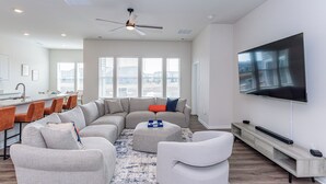 A modern living room with a sectional sofa, ottoman, and a flat-screen TV mounted on the wall. - 4 bed, 3 bath Single Family Home in Millville by the Sea: Community Pool, Fitness Center, Club house, Kayaking, Beach Shuttle, Free WIFI (Frankford)