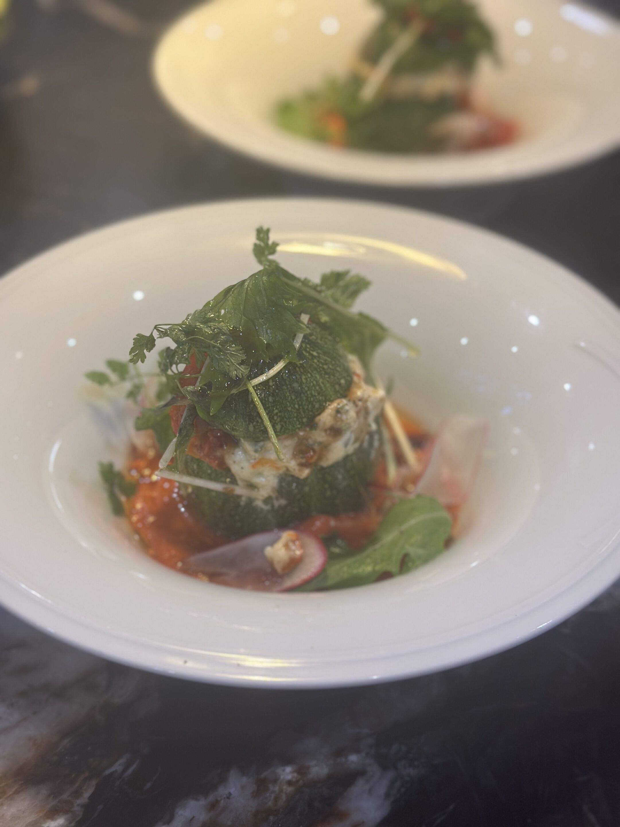 A white plate with a food dish, possibly a salad or appetizer, with greens and a red sauce.