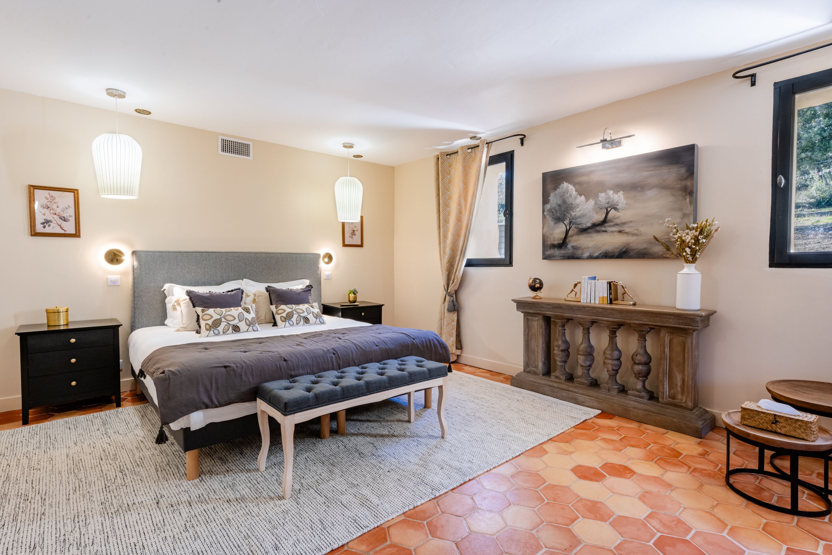 A bedroom with a bed, bedside tables, a bench, a dresser, and a painting on the wall.