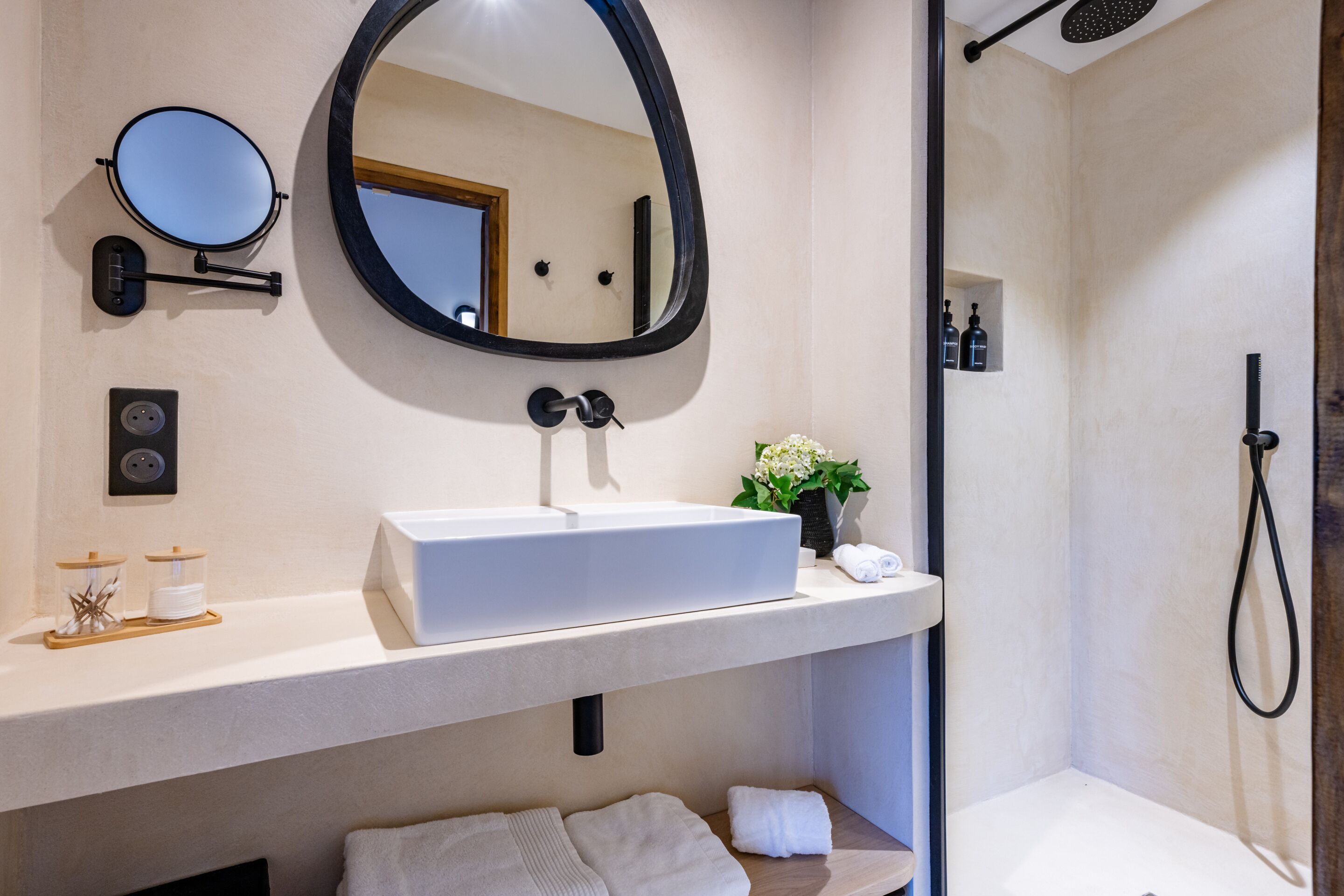 A modern bathroom with a white sink, a round mirror, and a shower.