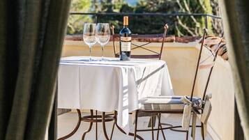 A table set for two with a bottle of wine and two glasses, overlooking a garden with trees.