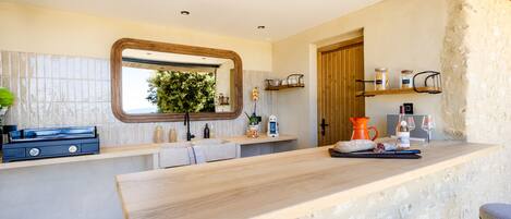 A modern kitchen with a wooden countertop, stone wall, and a window overlooking greenery.