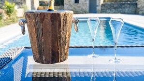 Un balde de madera con una botella de champán y dos copas sobre una mesa junto a una piscina.