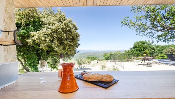 Una mesa de madera con vista a un paisaje montañoso, una jarrón y una hogaza de pan.