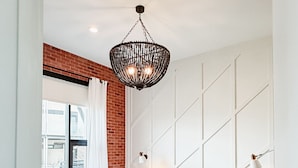 A modern bedroom with a large bed, a hanging light fixture, a brick accent wall, and a view of the city. - Lamar Treehouse (Austin)