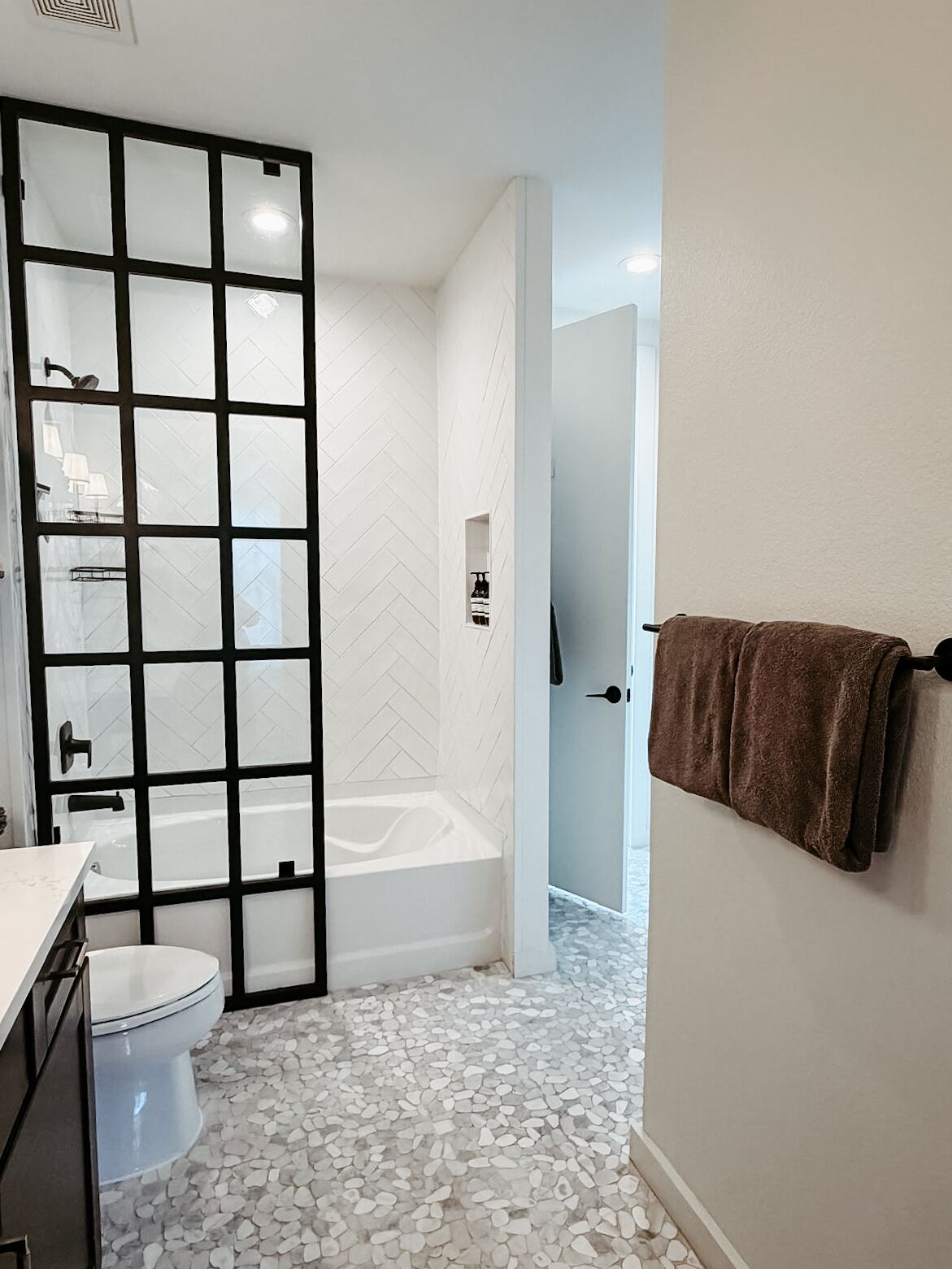 A bathroom with a white herringbone tile wall, a white bathtub, a white toilet, and a glass door leading to a shower area.