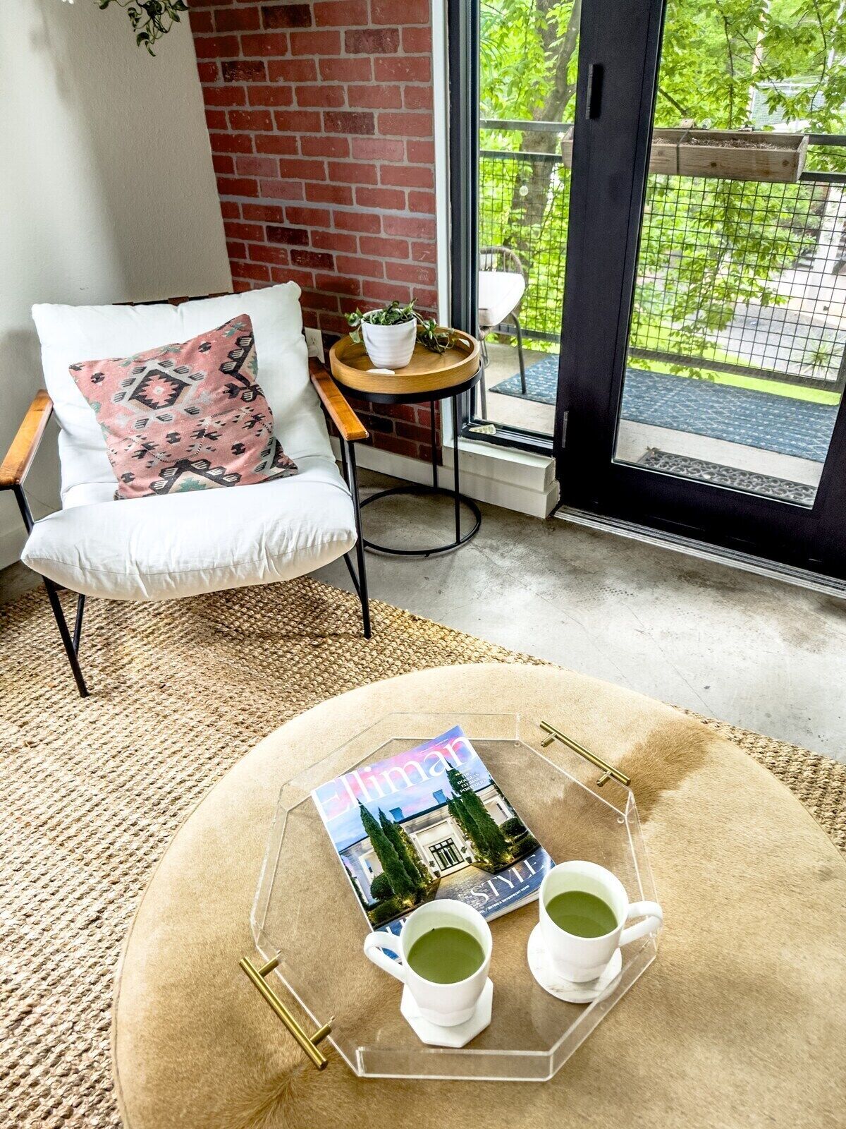 Een gezellige kamer met een witte stoel, een ronde tafel met een tijdschrift en twee kopjes groene thee, en uitzicht op groen buiten.