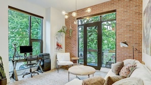 A modern office space with a large desk, computer, and chair, a round table, and a sofa with cushions. - Lamar Treehouse (Austin)