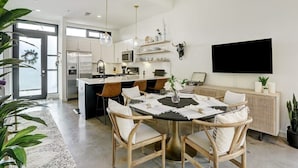 A modern kitchen with a central island, white cabinetry, and a dining area with a round table and chairs. - Lamar Treehouse (Austin)