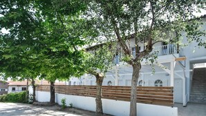 Un patio con un edificio blanco, bancos de madera y árboles que dan sombra.