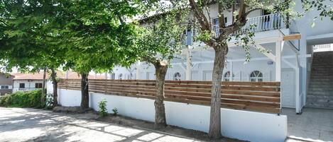 A courtyard with a white building, wooden benches, and trees providing shade.