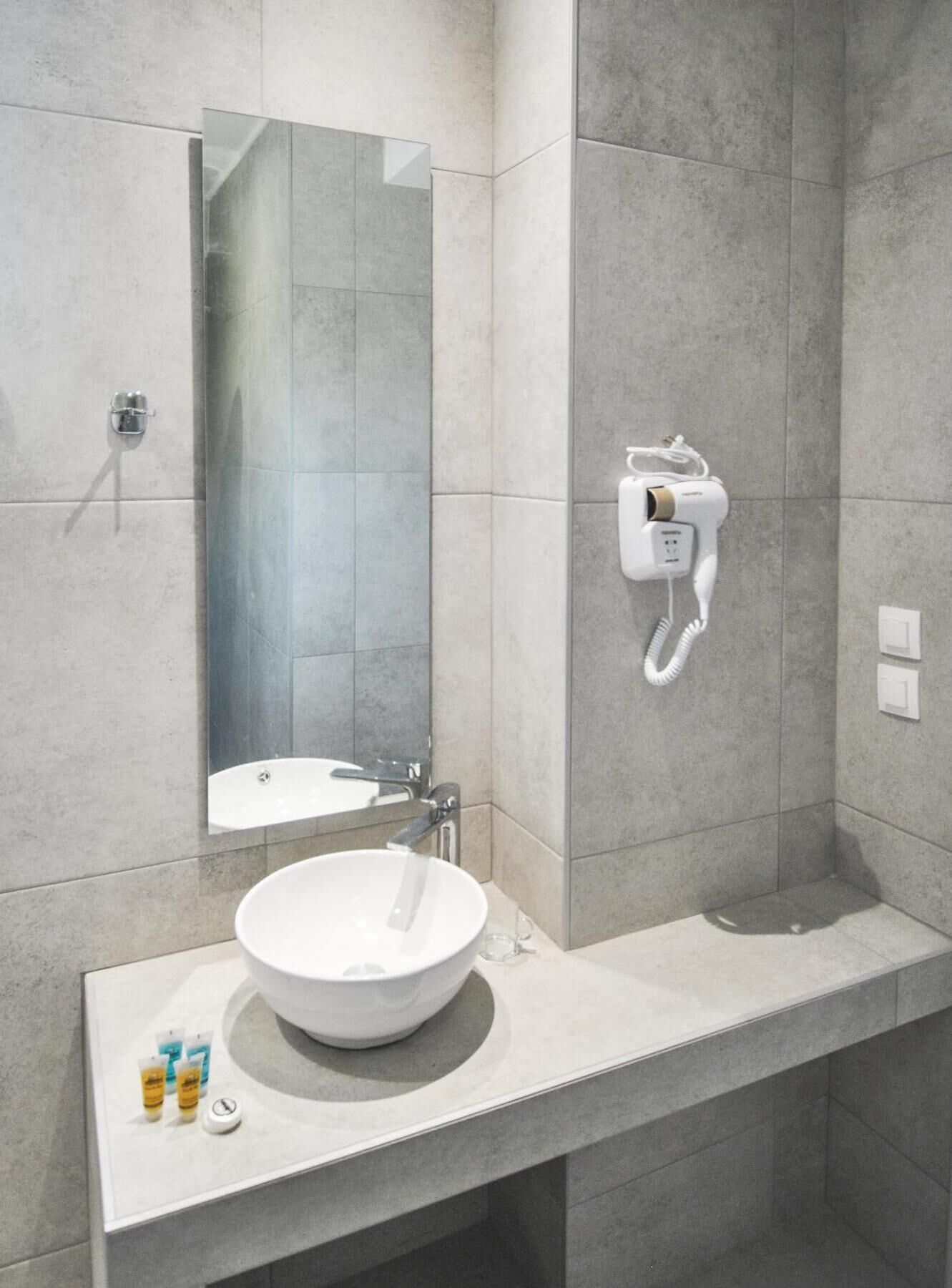 A modern bathroom with a large mirror, a white sink, and a hairdryer mounted on the wall.