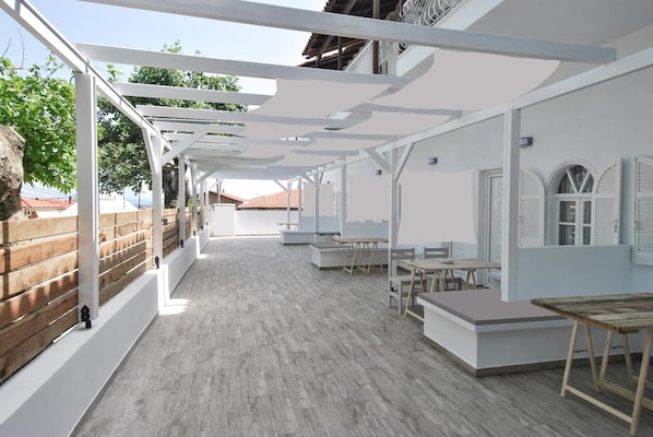 Un amplio espacio al aire libre con terraza de madera, pérgola blanca y conjuntos de asientos.