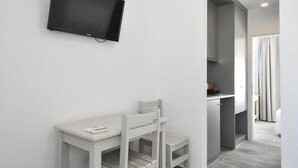Una habitación moderna y minimalista con un televisor blanco montado en la pared, una pequeña mesa blanca con dos sillas y un suelo de madera gris.