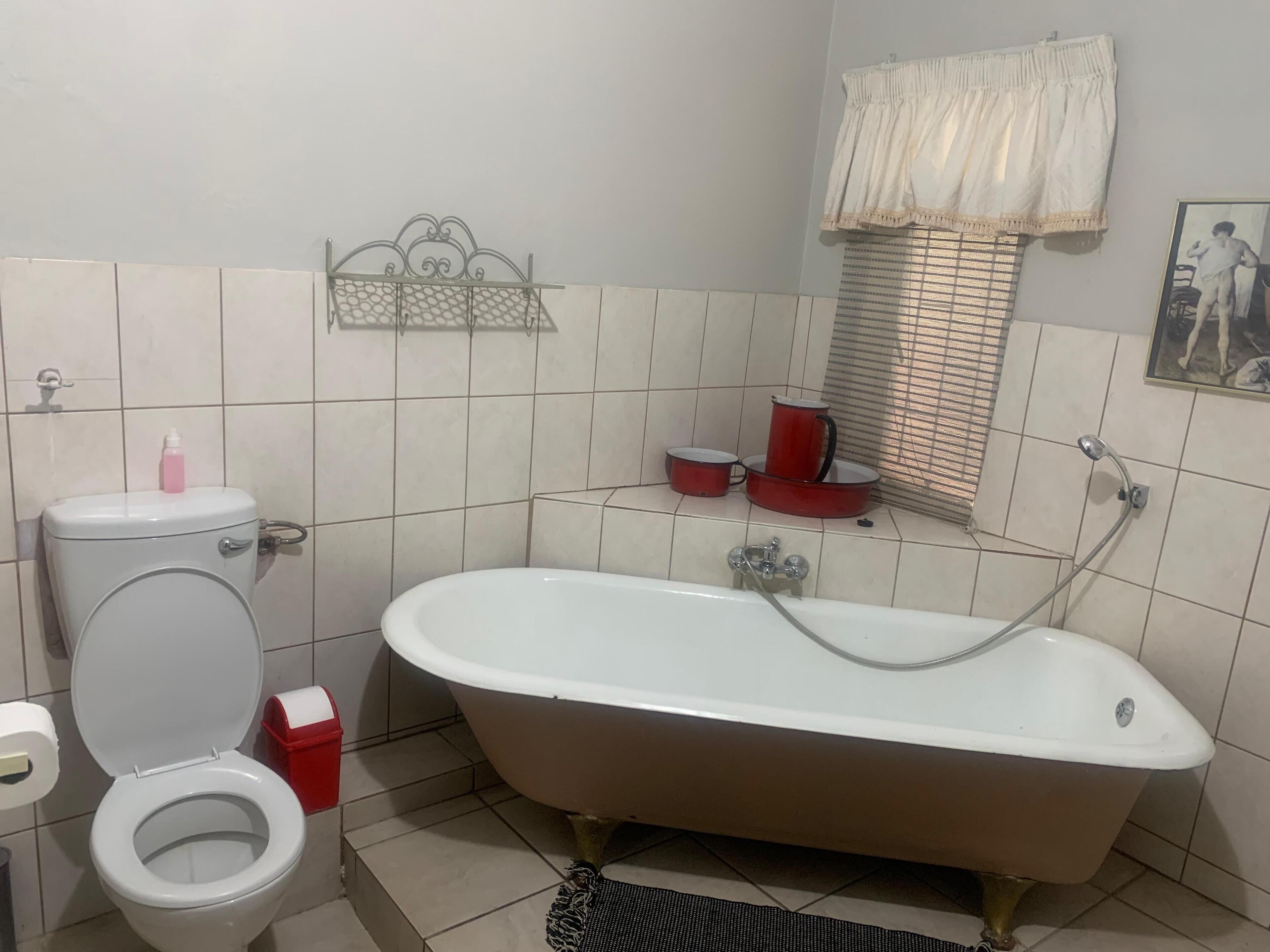 A bathroom with a toilet, a bathtub, and a window with blinds.