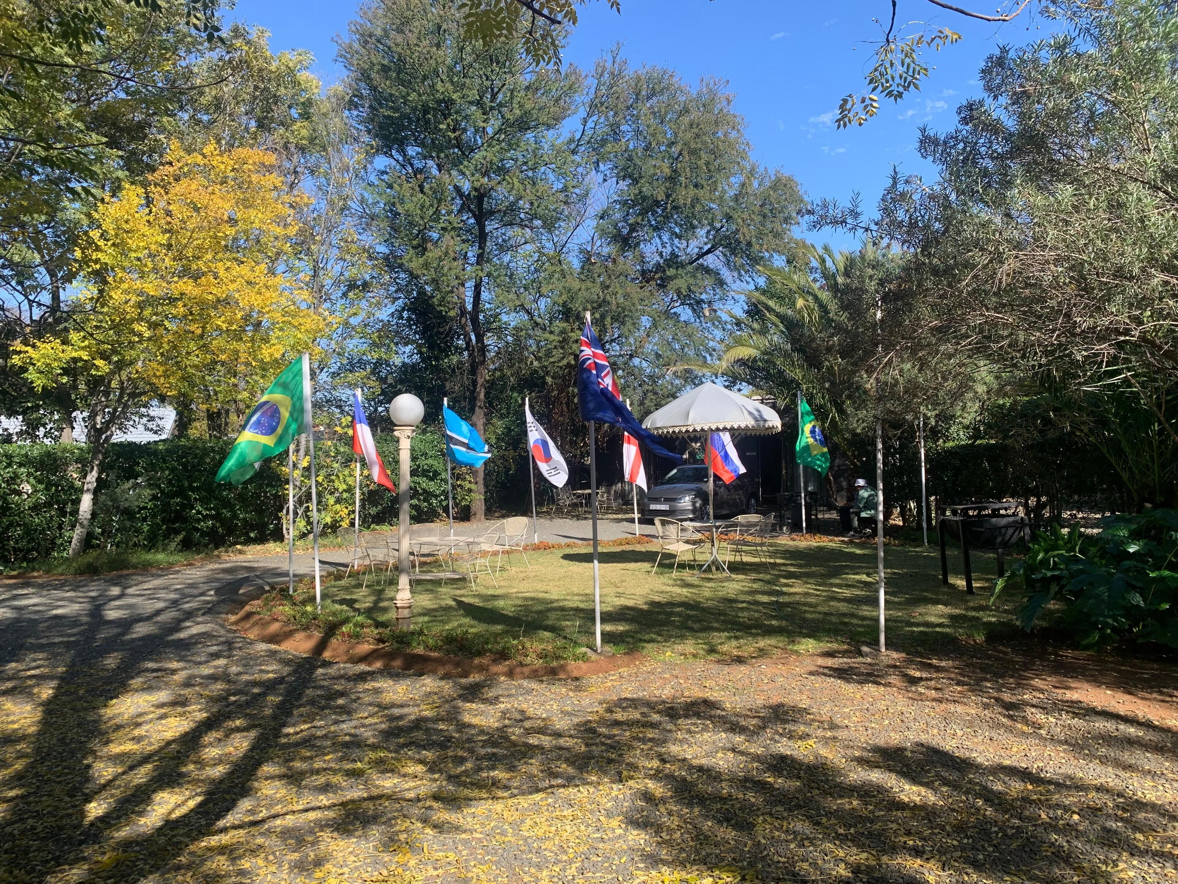 Un jardín con varias banderas, un pabellón y un coche aparcado al fondo.