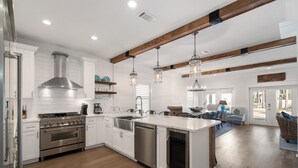A modern kitchen with white cabinetry, stainless steel appliances, wooden beams, and pendant lighting. - Sandy Cheeks - Stunning 4 Bedroom with 4 bikes & seconds to the Resort Pool! (Panama City Beach)