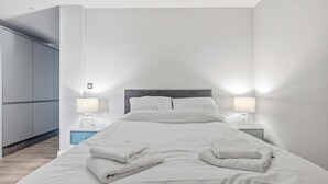 A modern bedroom with a large bed, two bedside tables with lamps, a wardrobe, and a blue nightstand. - Modern & Spacious Studio Apartment in Leicester (Leicester)