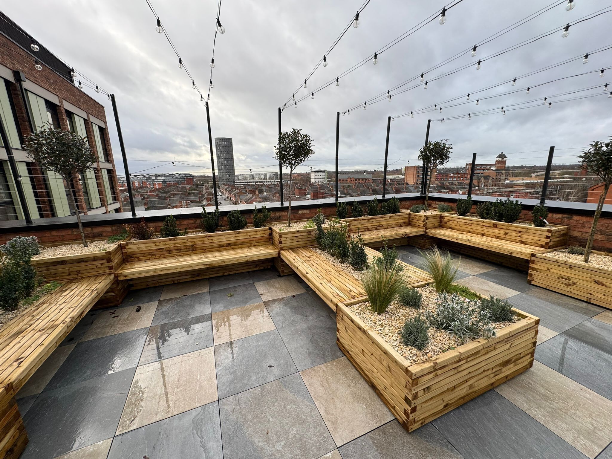 Eine Dachterrasse mit Holzpflanzgefäßen und Sitzmöglichkeiten, mit Blick auf die Stadt.