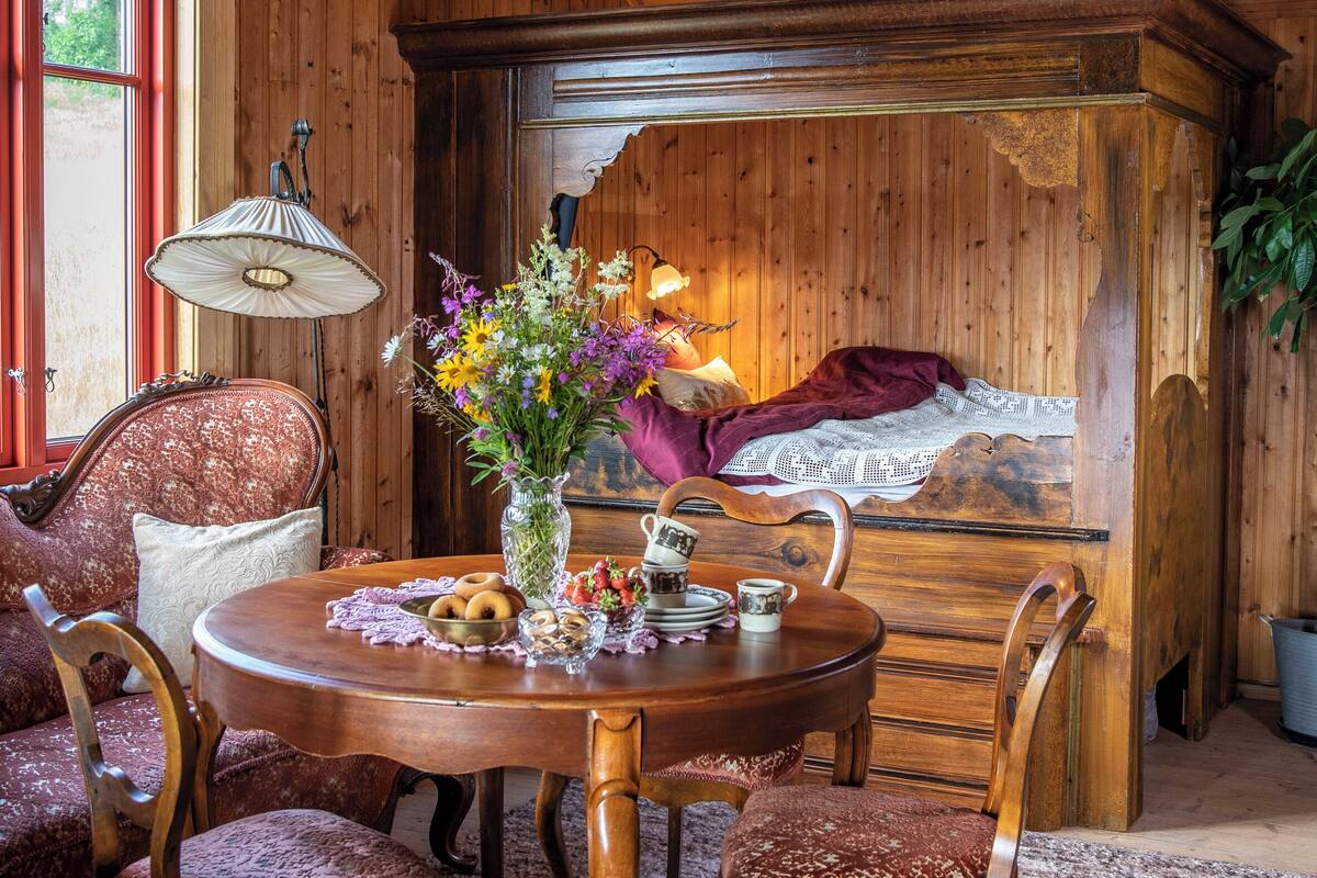 Comedor de madera con una mesa redonda, sillas, un florero con flores y una lámpara.
