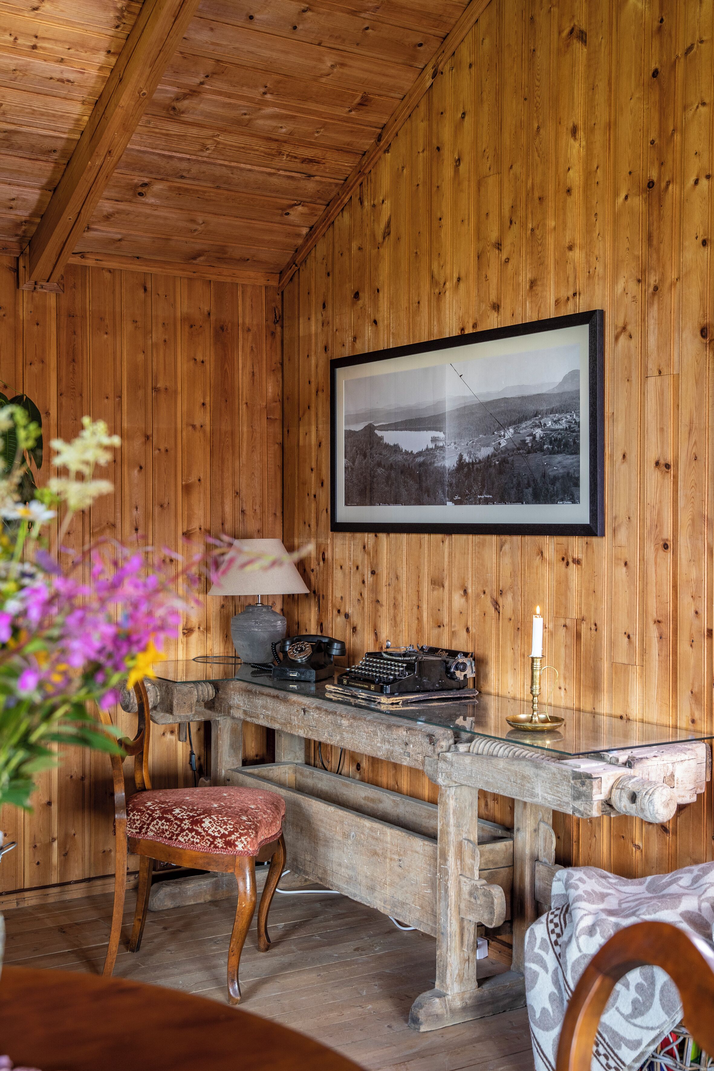 A wooden cabin interior with a desk, chair, lamp, and framed photograph on the wall.