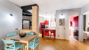 Een moderne keuken met een bakstenen zuil, een eethoek met een houten tafel en turquoise stoelen, en een rode accentmuur.