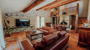 A rustic living room with stone walls, wooden beams, a television, leather sofas, and a fireplace. - Mas Sarava - Relaxation retreat, pilates & massage (Espira-de-l'Agly)