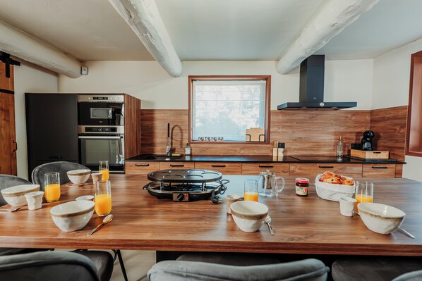 Una cocina moderna con una mesa de comedor preparada para el desayuno, incluyendo tazones, vasos y una estufa portátil.