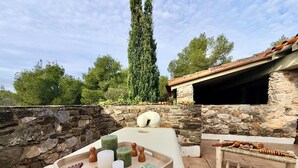 A stone wall with a stone bench, a tray with candles and wooden objects, and a view of trees and a building in the background. - Mas Sarava - Relaxation retreat, pilates & massage (Espira-de-l'Agly)