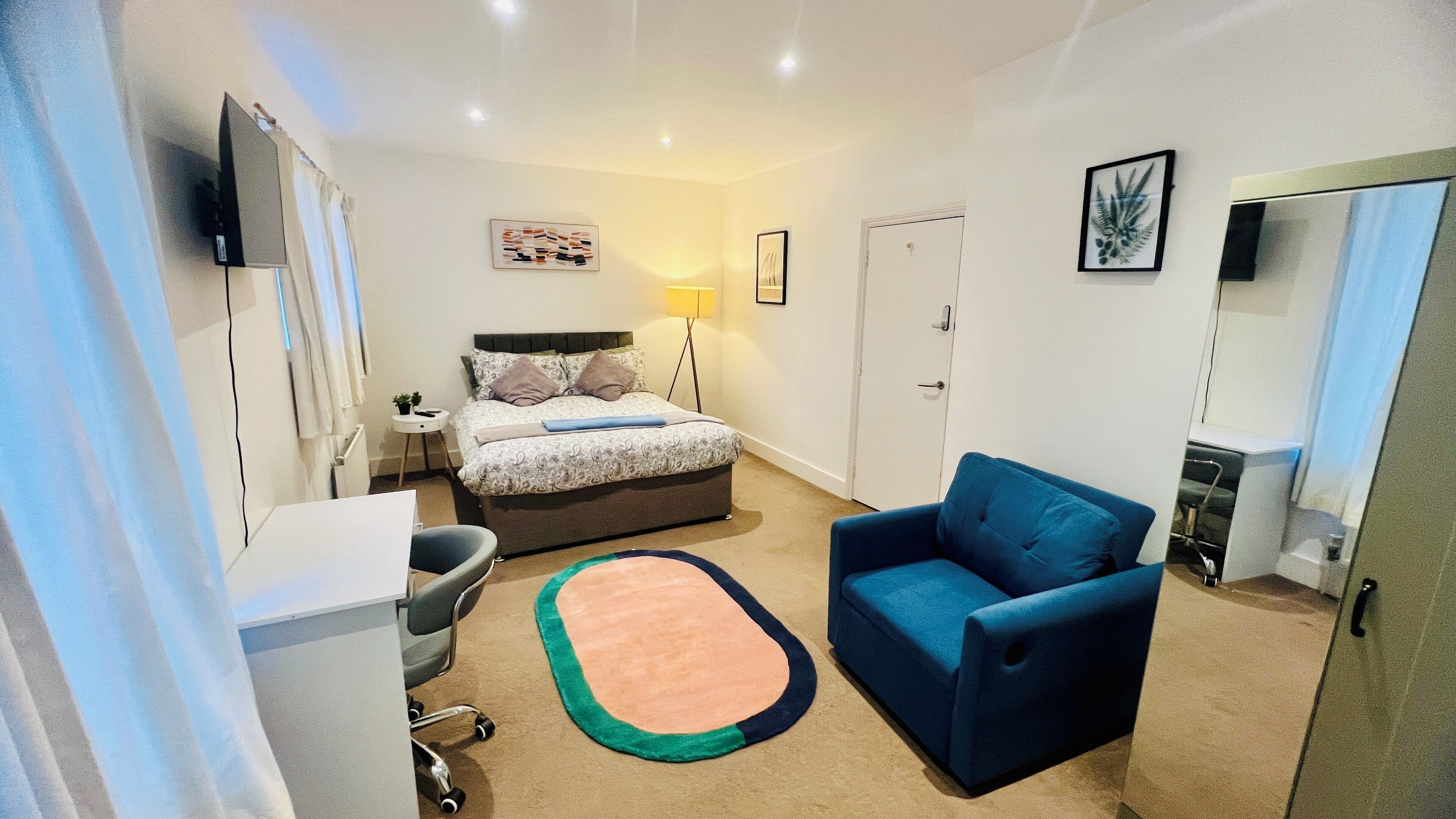 Un dormitorio compacto con cama, una silla azul, un escritorio y una alfombra pequeña.