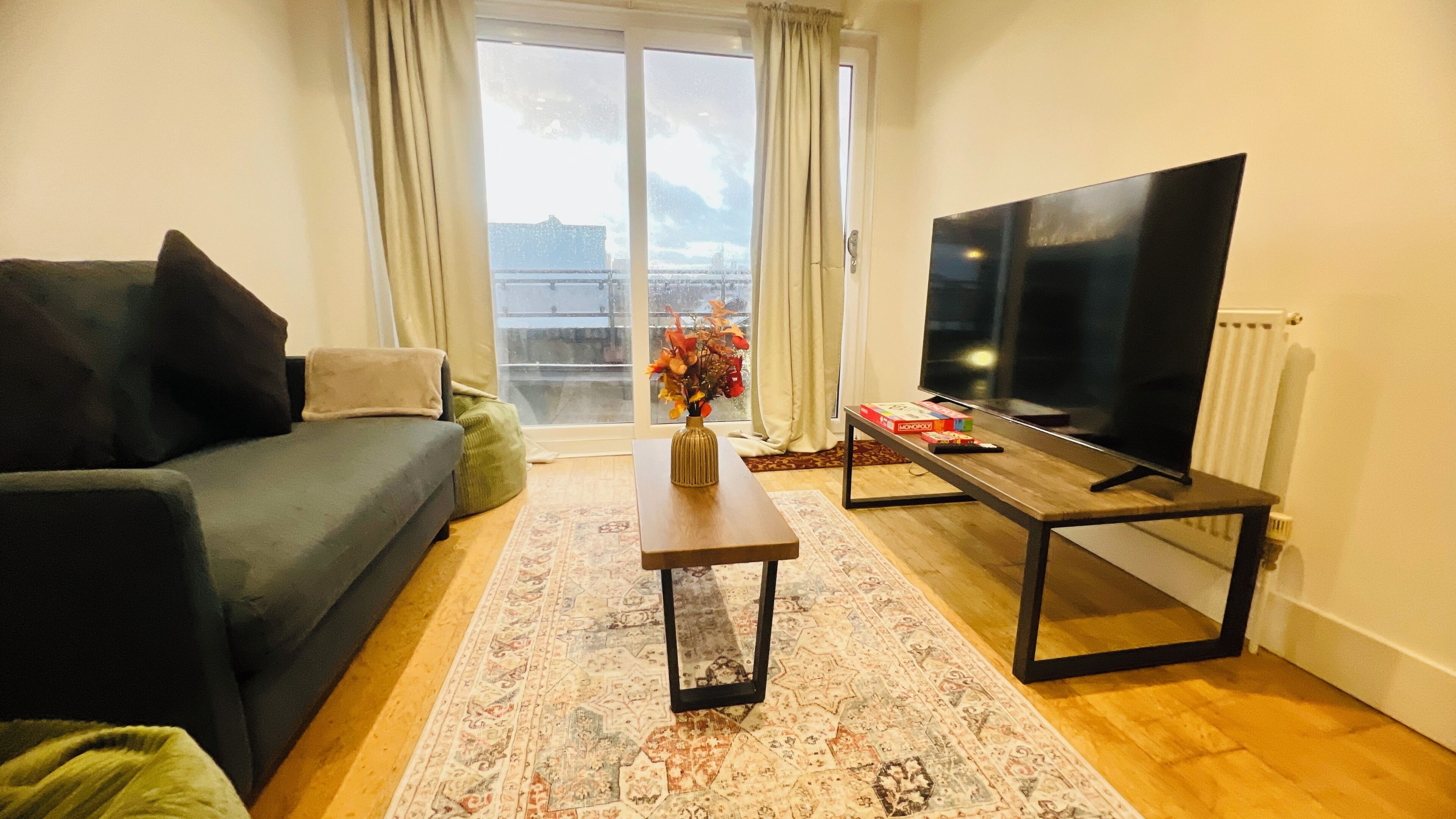 A living room with a sofa, a coffee table with a vase, a TV on a stand, and a view through a window.