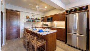 Una cocina moderna con una isla central, armarios de madera, un refrigerador de acero inoxidable y un ventilador de techo.