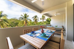 A balcony with a wooden table set for dining, chairs, and a ceiling fan.