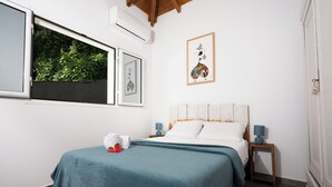 Ein Schlafzimmer mit Bett, einem Fenster mit Blick auf Grünflächen, einem gerahmten Kunstwerk und einem Nachttisch mit Lampe.