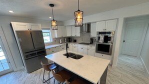 A modern kitchen with white cabinetry, a central island with bar stools, stainless steel appliances, and pendant lighting. - Modern South Tampa Retreat steps off Bayshore blvd, the bay is a minute away (Tampa)