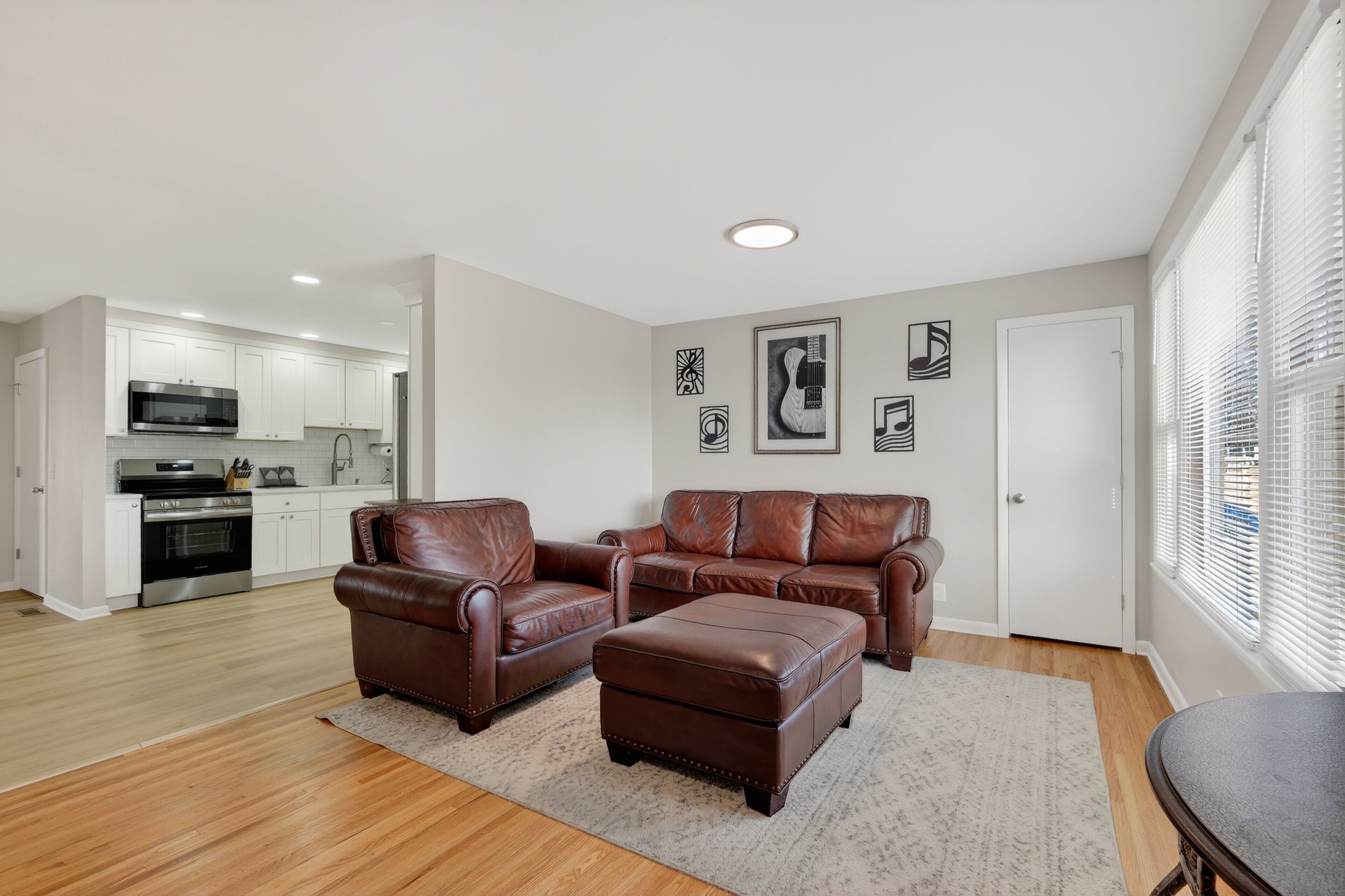A modern living room with a brown leather sofa set, a dining table, and a kitchen in the background.