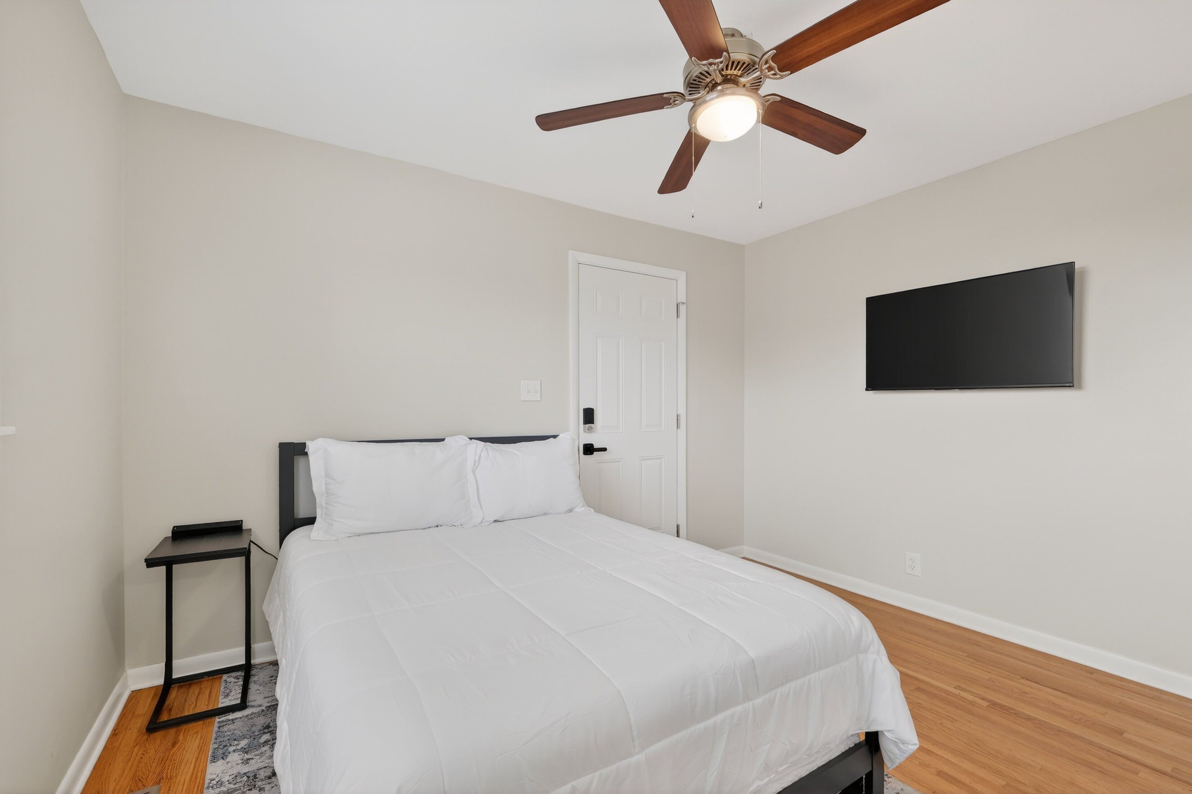 A bedroom with a bed, a ceiling fan, a TV, and a door.